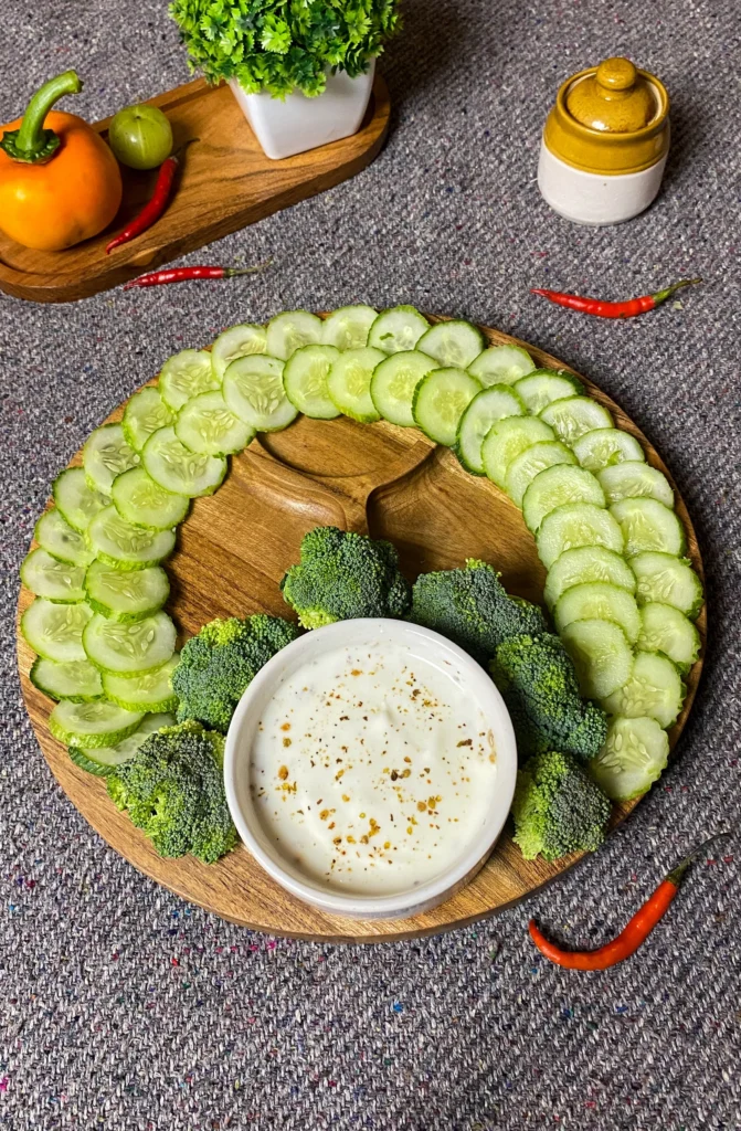 Healthy appetizer on wooden plate with fresh cucumber slices, broccoli florets, and creamy seasoned yogurt dip, perfect for light party snacks